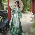 Elegant Women's Hanfu cosplay in green dress with floral details, styled with a parasol in a serene outdoor setting.