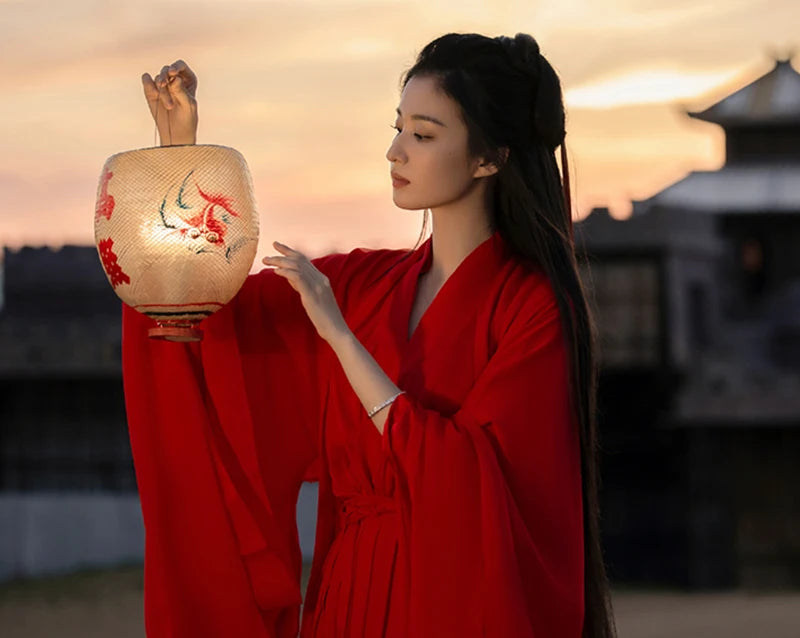 Woman in a red Hanfu dress holding a lantern at sunset, showcasing traditional Chinese style.