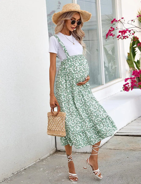 Maternity dress in green floral print, perfect for summer, worn by pregnant woman with a straw hat and stylish accessories.