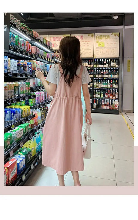 Woman wearing a pink loose fit maternity dress in a store aisle with beverages.
