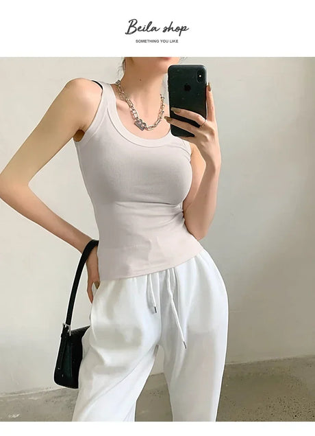 Woman modeling a sleeveless ribbed tank top with a stylish necklace and white joggers, perfect for streetwear.