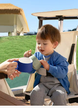 Child enjoying playtime with colorful cups in a lightweight travel stroller on a sunny day.