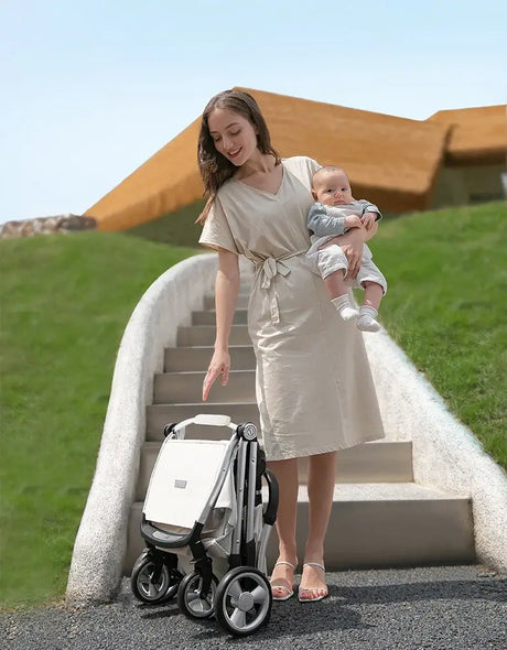 Mom joyfully holds baby while standing next to a twin baby stroller on a staircase outdoors.