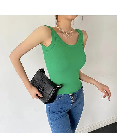 Stylish woman wearing a green sleeveless ribbed tank top with a black handbag, paired with blue jeans.