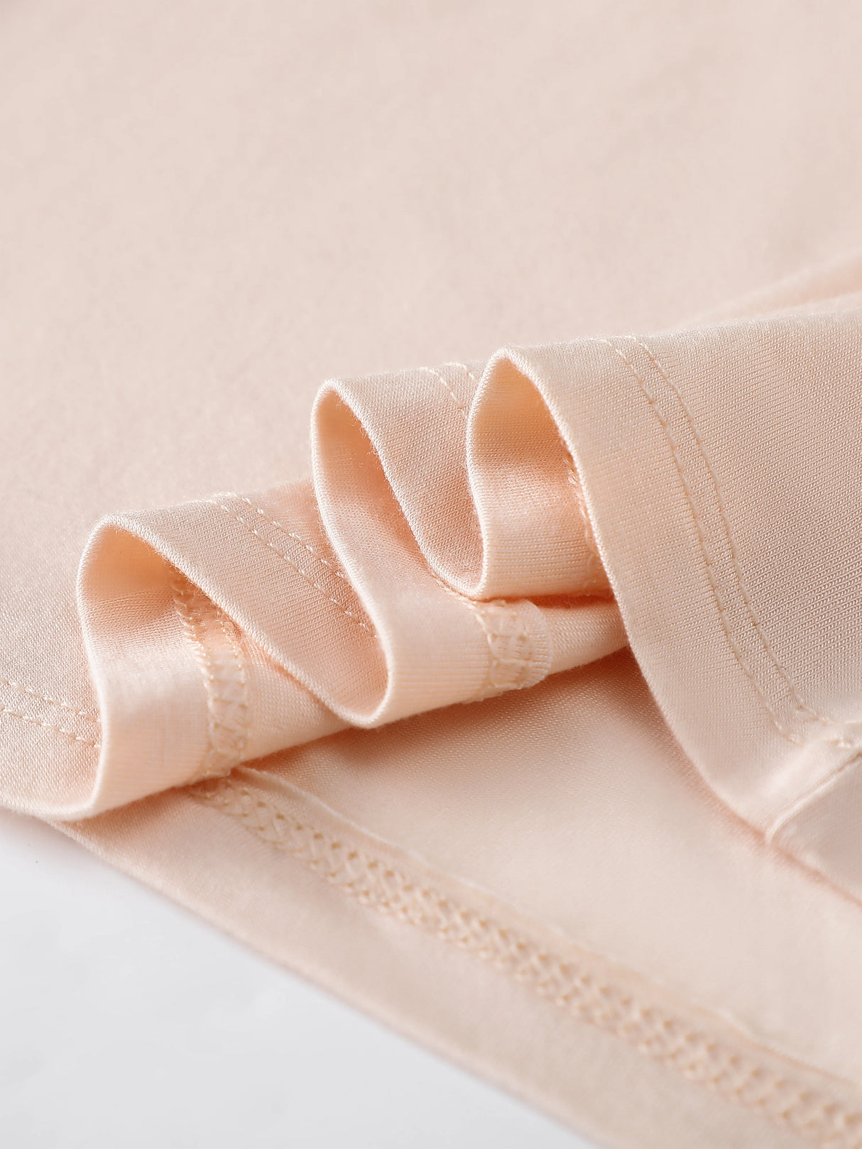 Close-up of soft peach fabric showing folded edges of a Bralux™ camisole, highlighting its smooth texture and quality stitching.