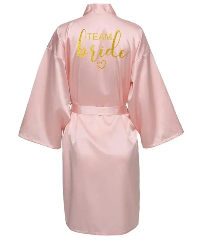 Pink satin robe for brides with 'TEAM bride' in glittery gold lettering on the back.