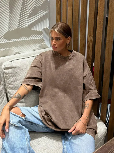 Woman wearing a loose-fitting brown casual t-shirt while sitting on a sofa in a stylish interior.