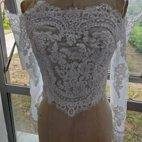 Lace off shoulder bridal jacket with intricate appliqued design and long sleeves, perfect for wedding attire.