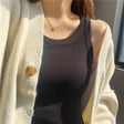 Close-up of a woman wearing a black padded cotton spaghetti camisole under a cozy cream cardigan.
