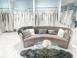 Elegant bridal boutique interior featuring wedding gowns, a cozy curved sofa, and decorative pillows.
