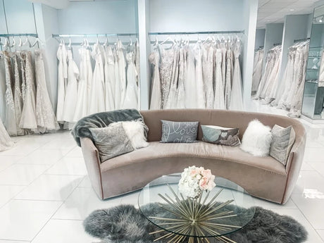 Elegant bridal shop interior with a plush curved couch and a backdrop of white wedding dresses hanging on racks.