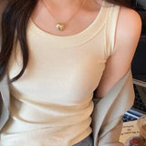 Close-up of a woman wearing a beige padded cotton spaghetti camisole, styled with a gold heart necklace.
