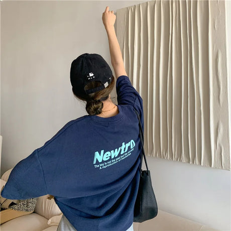 Young woman wearing an oversized navy Harajuku streetwear tee with a trendy cap, showcasing a casual street style.