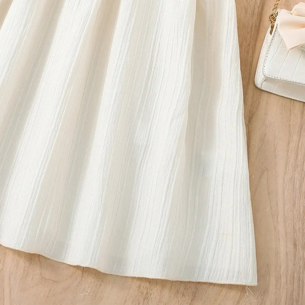 Light cream-colored dress fabric with textured finish on wooden surface.