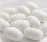Close-up of white silk cocoons on a pale background, showcasing their soft texture and natural form.
