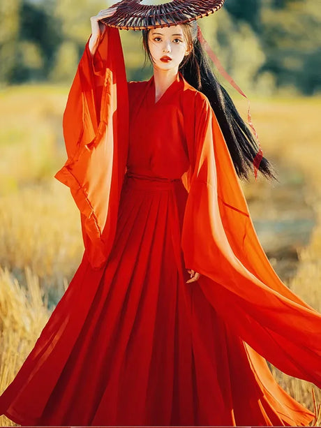 Woman in vibrant red hanfu costume with wide sleeves and a traditional hat, set against a natural background.