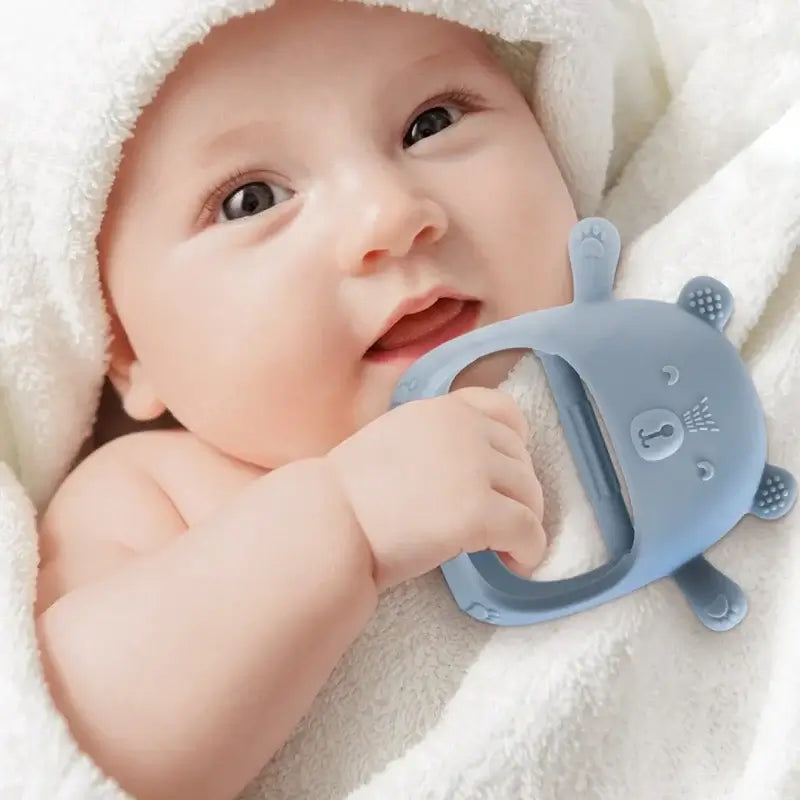 Smiling baby holding a soft silicone teether glove, wrapped in a towel, showcasing comfort and safety.