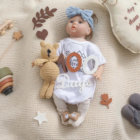 Baby doll with milestone card, soft toy, and decorative elements on a cozy knit blanket.