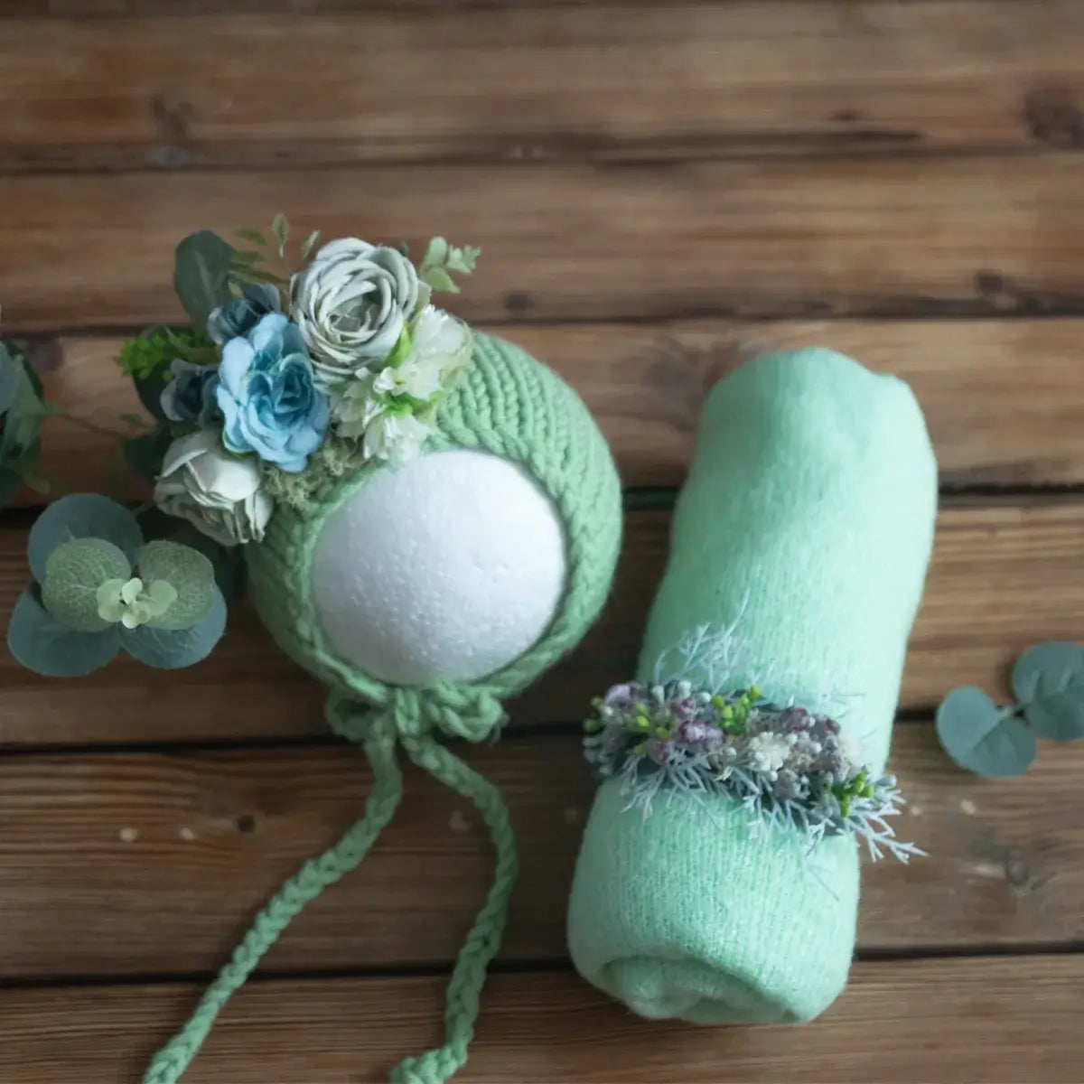 Newborn stretch knit mohair hat with floral decorations and matching green wrap on wooden background.