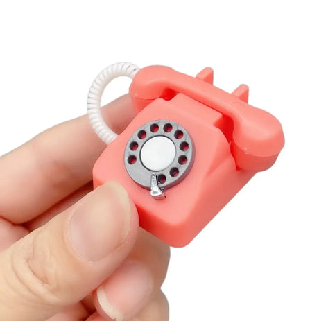 Miniature pink rotary phone held in hand, perfect for photography props or as a cute decorative item.