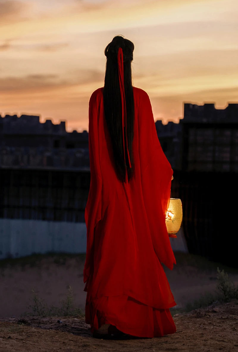 Woman in a red Hanfu dress holding a lantern, against a sunset backdrop, showcasing traditional Chinese cosplay attire.