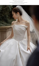 Lace off shoulder bridal jacket with long sleeves featured on a bride wearing a satin wedding dress in an elegant setting.