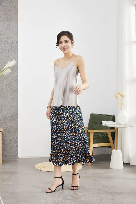 Woman in a silk camisole and floral skirt, showcasing summer fashion in a stylish indoor setting.