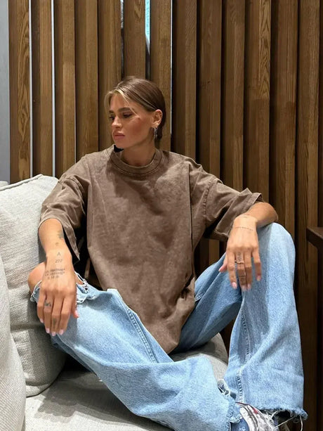 Casual brown oversized t-shirt worn by a woman sitting comfortably, paired with distressed jeans in a cozy setting.