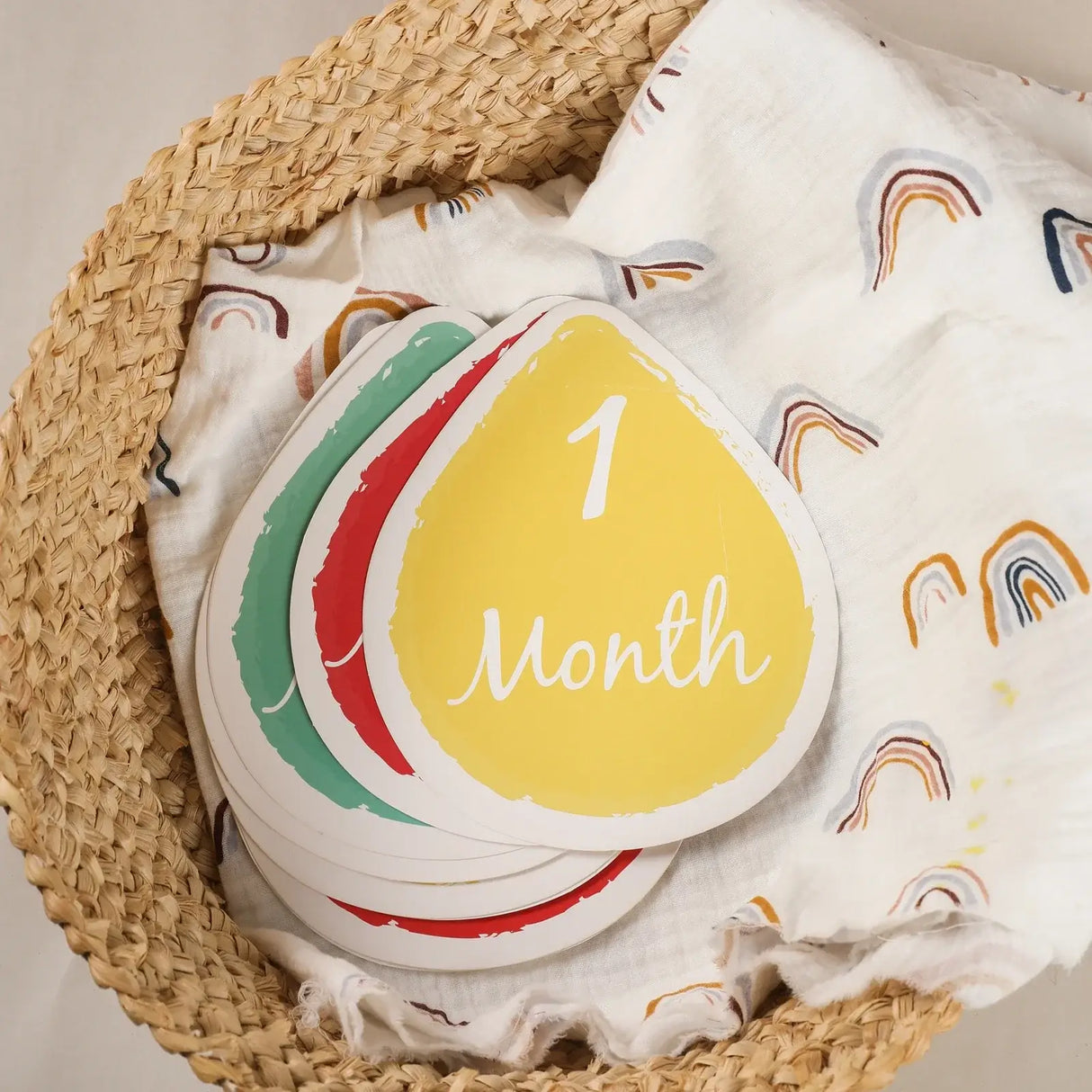 Colorful milestone cards for newborns displaying '1 Month' in a woven basket with soft fabric background.