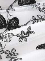 Close-up of intricate black lace pattern on white fabric, featuring flowers and butterfly designs.