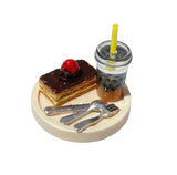 Miniature dessert scene featuring layered chocolate cake with a cherry and a drink with a straw on a plate.