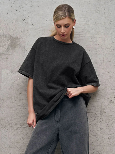 Model wearing a black Wolfeel Wax Printed Casual T-Shirt paired with loose gray trousers against a concrete background.