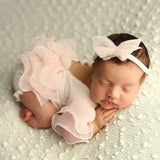 Adorable newborn wearing a pink ruffle outfit and headband, peacefully sleeping on a textured blanket.