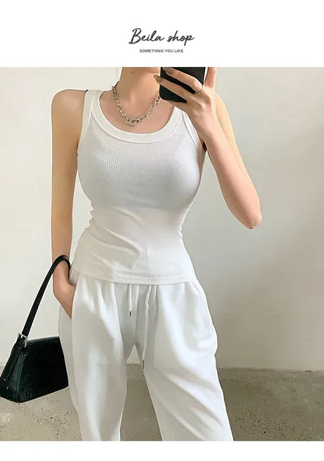 Model wearing a white sleeveless ribbed tank top paired with white pants, showcasing a casual streetwear style.