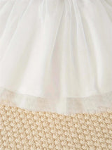 Close-up of a white tulle skirt detail on a textured beige background, perfect for newborn girls' summer dresses.