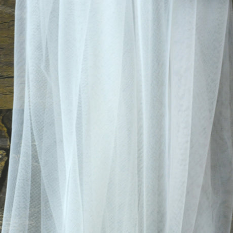 Close-up of sheer white fabric, perfect for bridal wraps or wedding jackets, showcasing delicate transparent tulle texture.
