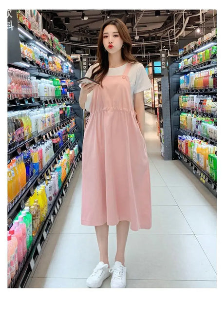 Woman in a pink loose fit maternity dress shopping in a store aisle filled with beverages.