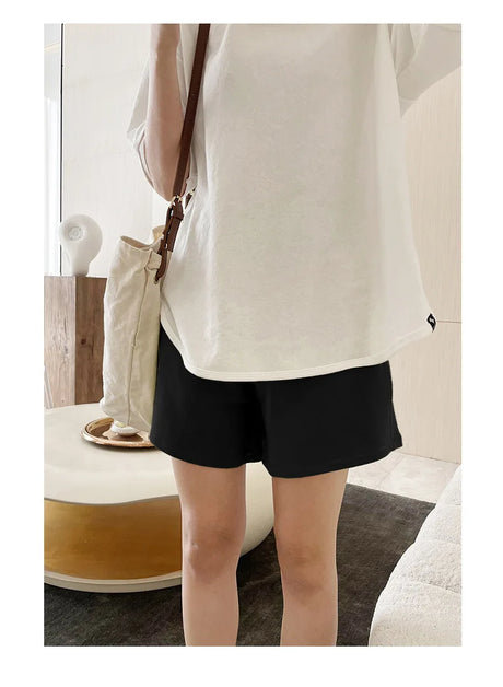 Model wearing plus size adjustable maternity shorts paired with a casual white top and handbag in a modern setting.