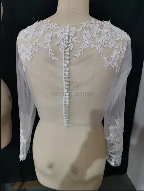 Lace bridal bolero with long sleeves and appliqued design, showcasing elegant back button details by Noble Weiss.