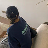 Woman wearing a navy oversized sweater with 'Newtro' print and a black cap, seated in a cozy room setting.