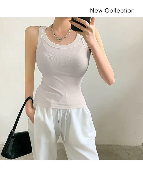 Woman wearing a sleeveless 90s vintage ribbed tank top in beige, paired with white pants and a black handbag.