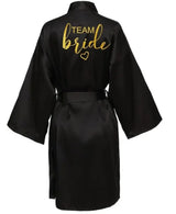 Black satin kimono robe with 'TEAM bride' in gold lettering, perfect for wedding parties.