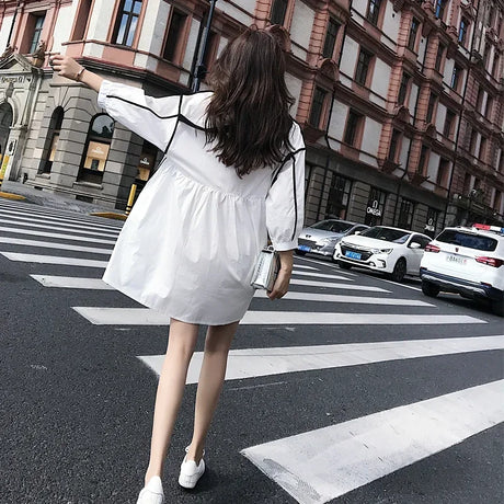 Woman wearing a white solid color maternity shirt dress walking in the city on a sunny day.