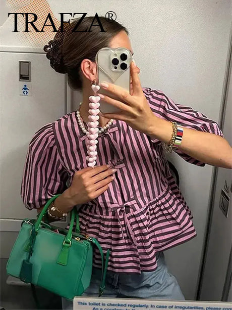 Woman wearing TRAFZA stripe lace-up blouse with green handbag and accessories in stylish setting.