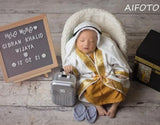 Baby boy dressed in a creative mini suitcase outfit, resting peacefully with a sign displaying his name and date.