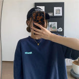A young woman wearing an oversized navy Harajuku streetwear tee with the text 'Newton' reflected in a mirror.