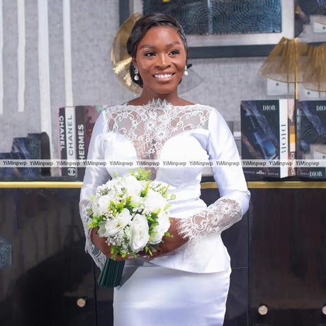 Elegant bride in lace long sleeve gown holding a bouquet, showcasing floral embroidery and satin fabric.