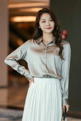 Woman in a stylish long sleeve silk shirt with a v-neck, paired with a pleated skirt, showcasing elegant fashion.