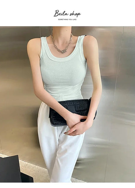 Woman wearing a light green sleeveless ribbed tank top, holding a black clutch, styled in a modern streetwear look.