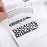 Hand holding a small white laptop mirror resembling a MacBook Air, featuring a realistic keyboard design.